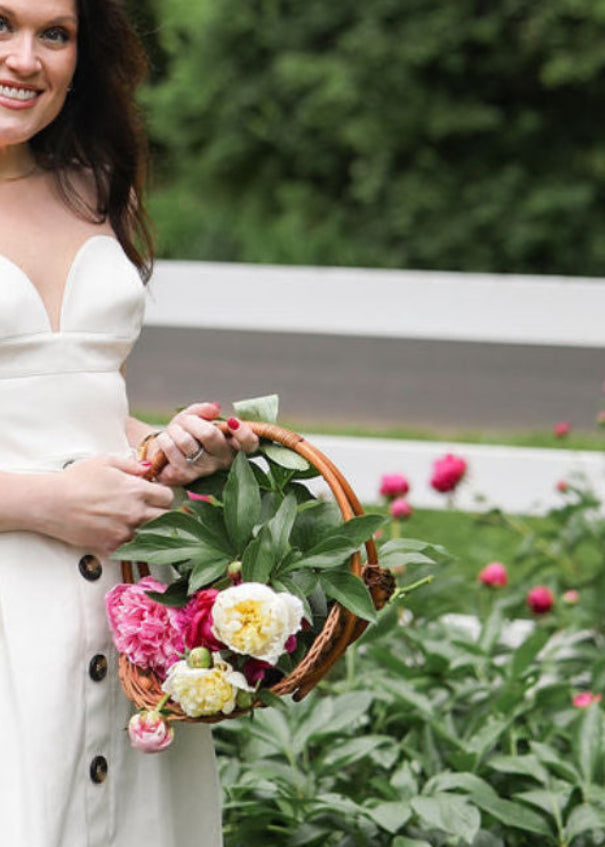 Woman in a white dress holding a basket of flowers outdoors