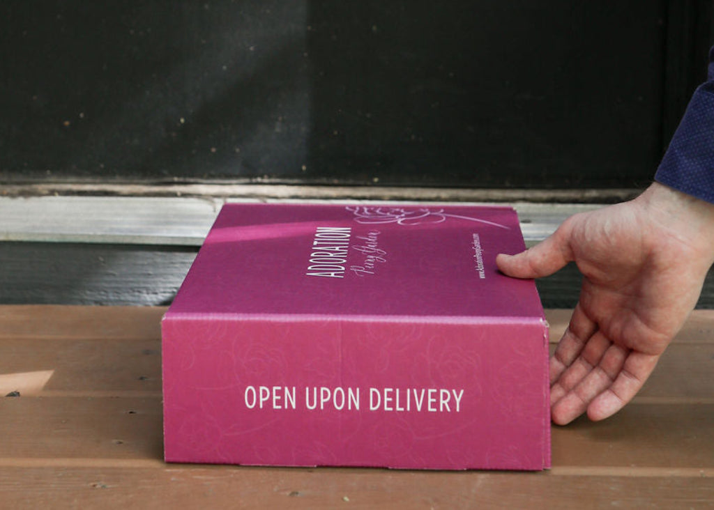 Hand picking up a pink delivery box from front door.